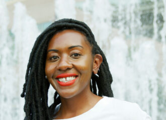 Portrait of Arissa smiling in front of a waterfall wearing a white shirt and red lipstick